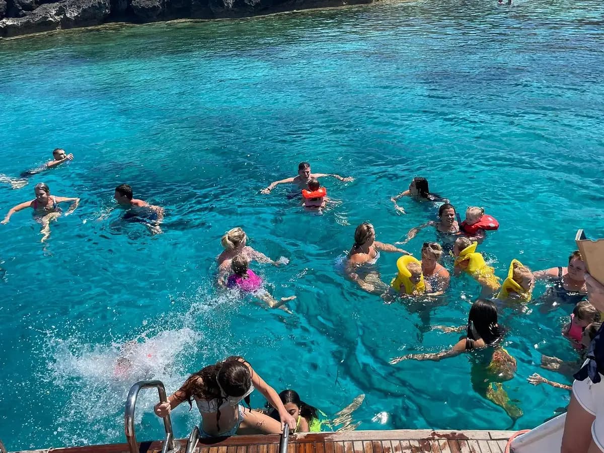 Adults and children swimming beside a boat as a passenger climbs the ladder